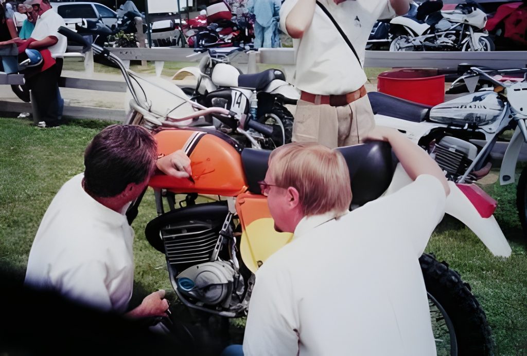 Men examining vintage motorcycles at outdoor event.