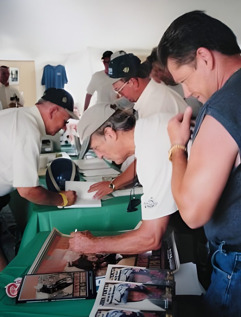 People signing autographs at event table.