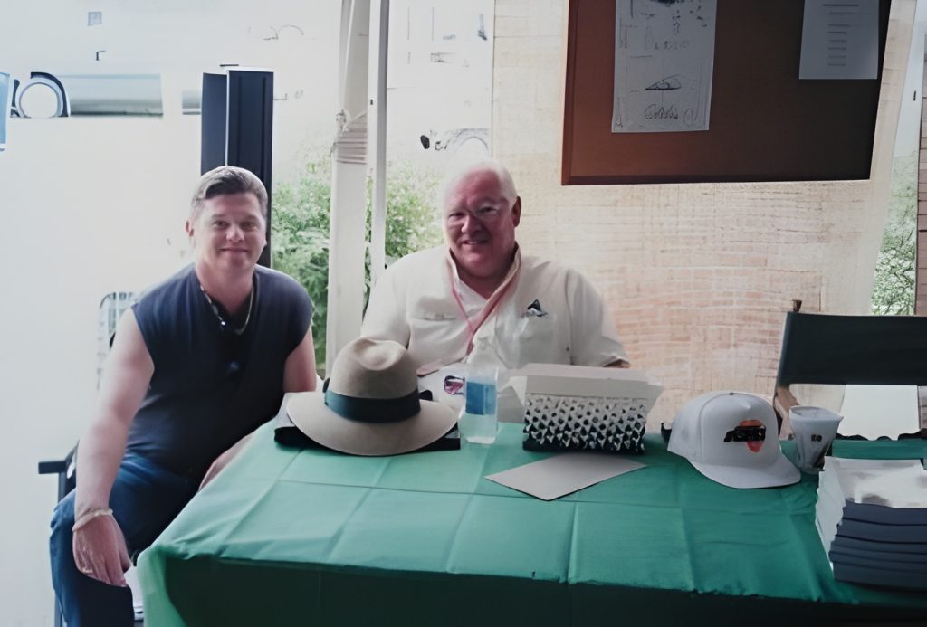 Two men sitting at a table, hats displayed.