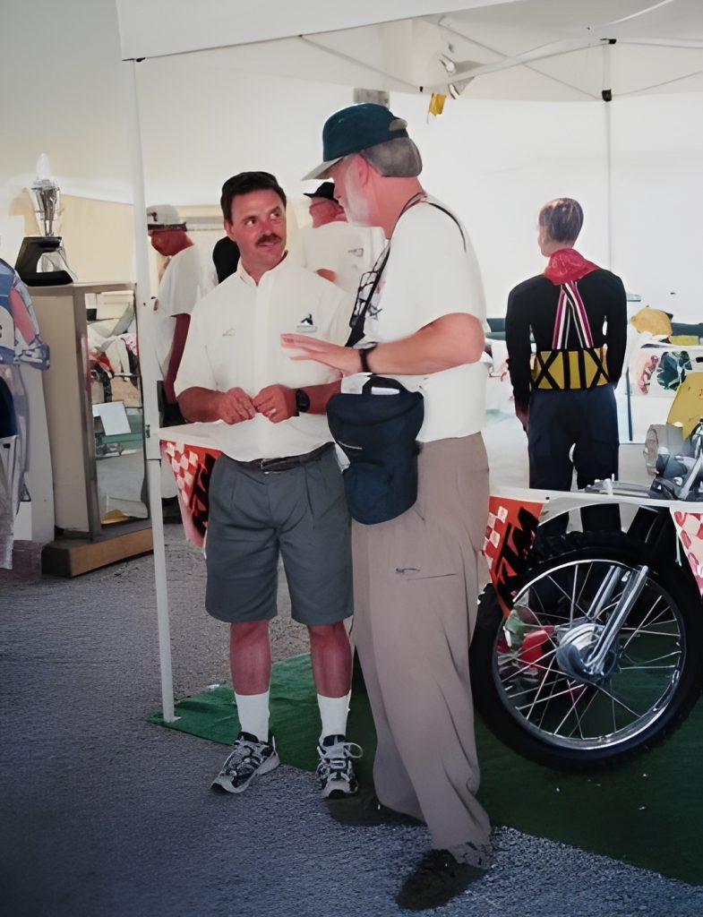 Two men conversing near a motorcycle exhibit.