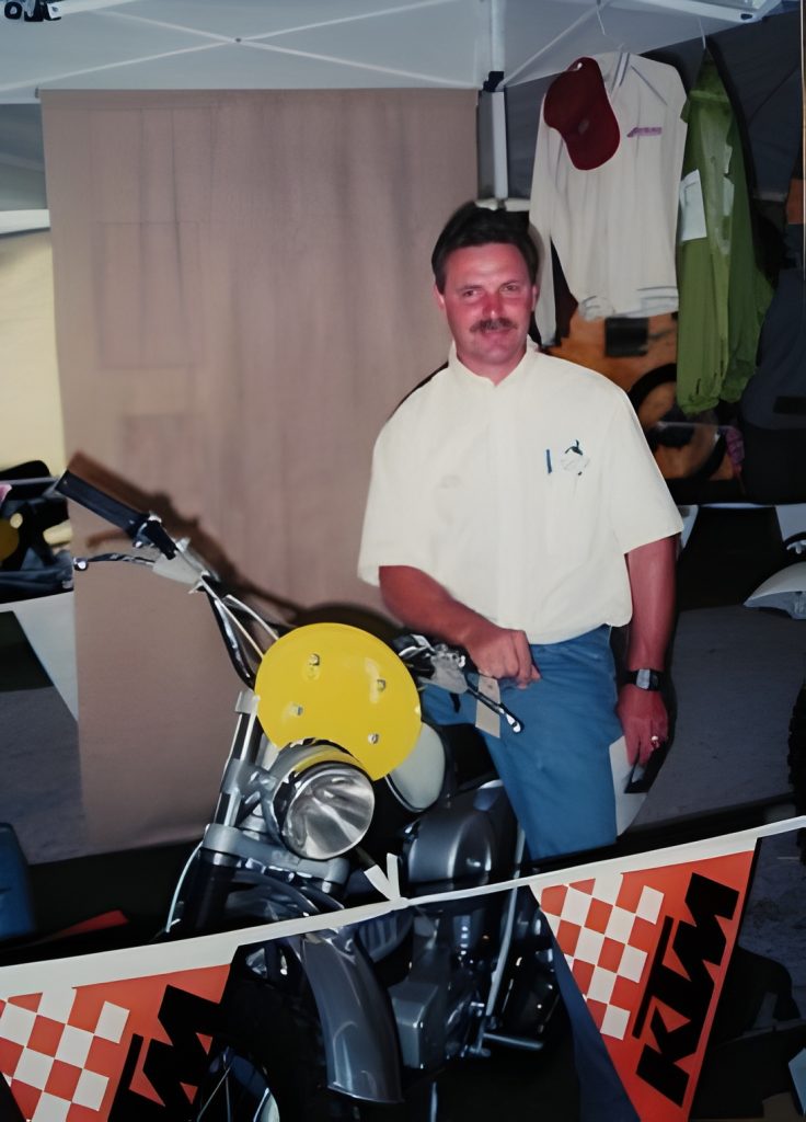 Man posing with vintage motorcycle at KTM event.