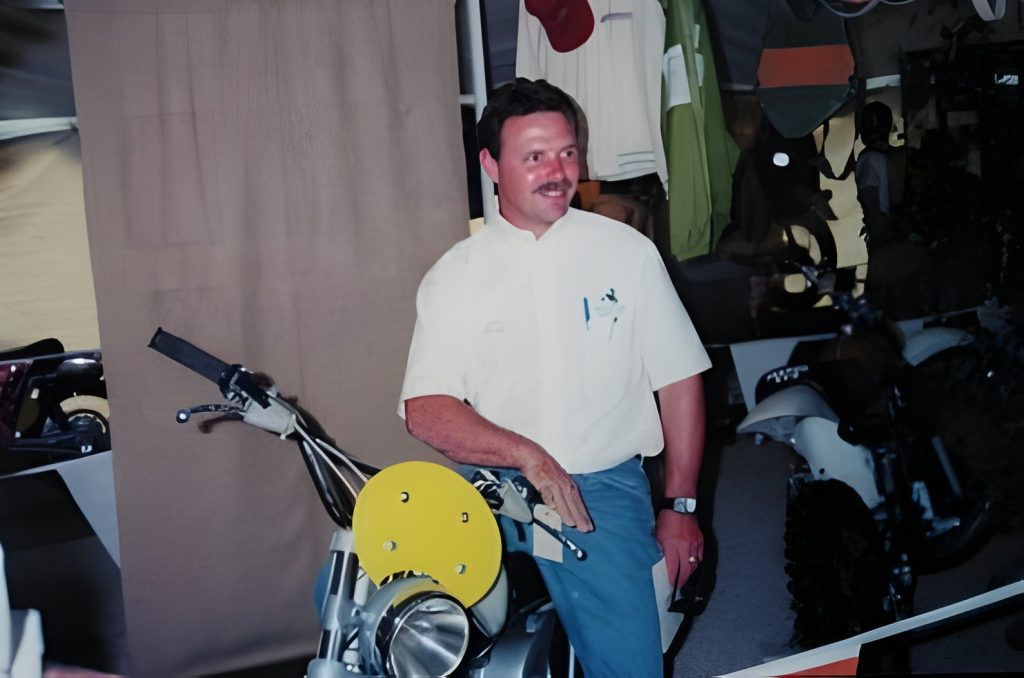 Man posing with motorbike at exhibition.