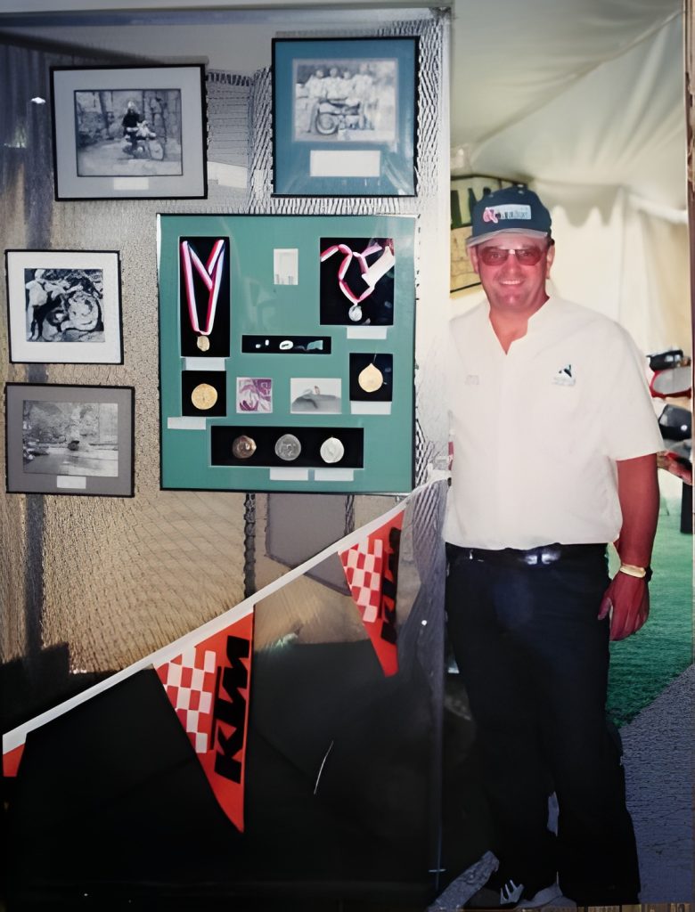 Man standing next to medals and photos display.