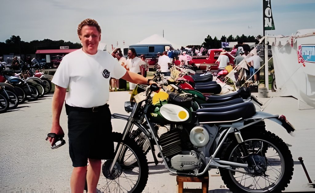 Man standing beside vintage motorcycles at outdoor event.