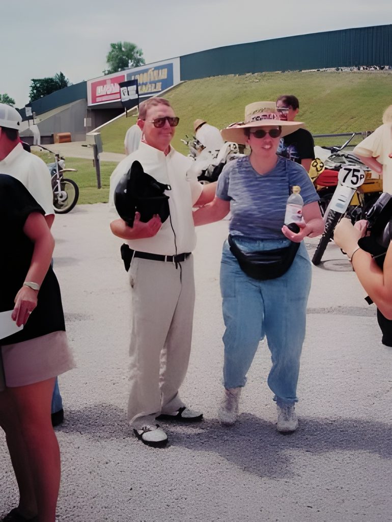 Couple at motorcycle event with hats and helmets.