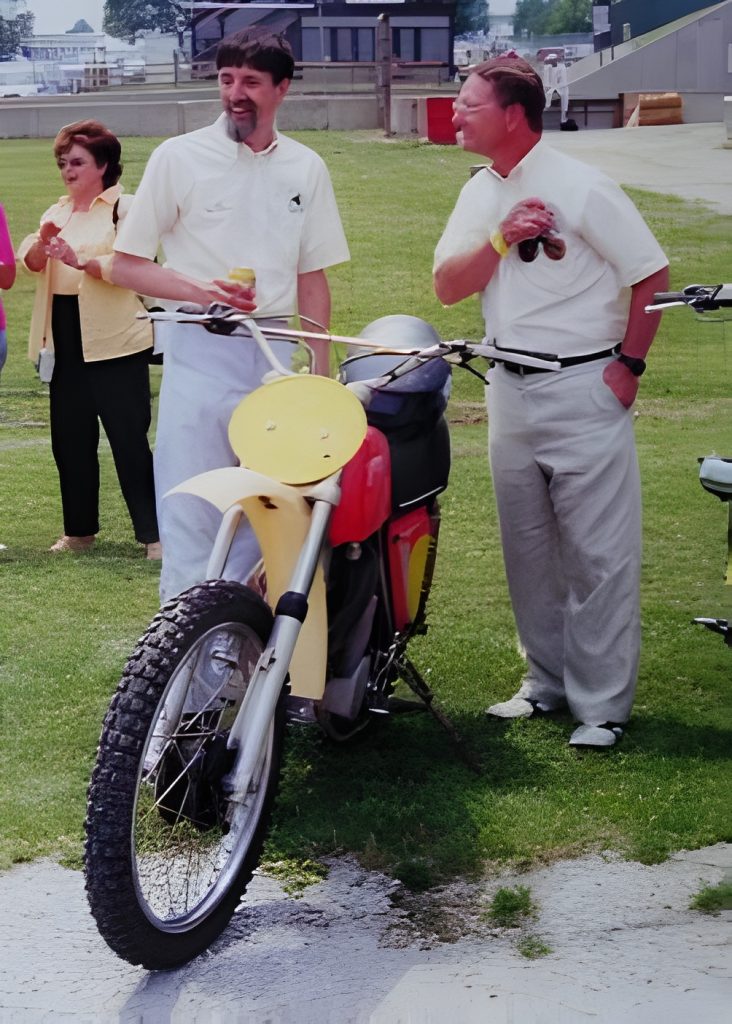 People standing beside a parked motorcycle on grass.