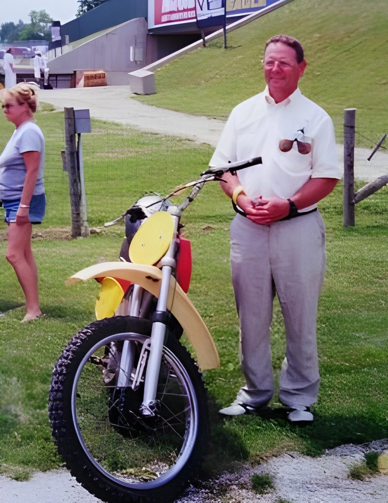 Man standing with motorcycle at outdoor event.