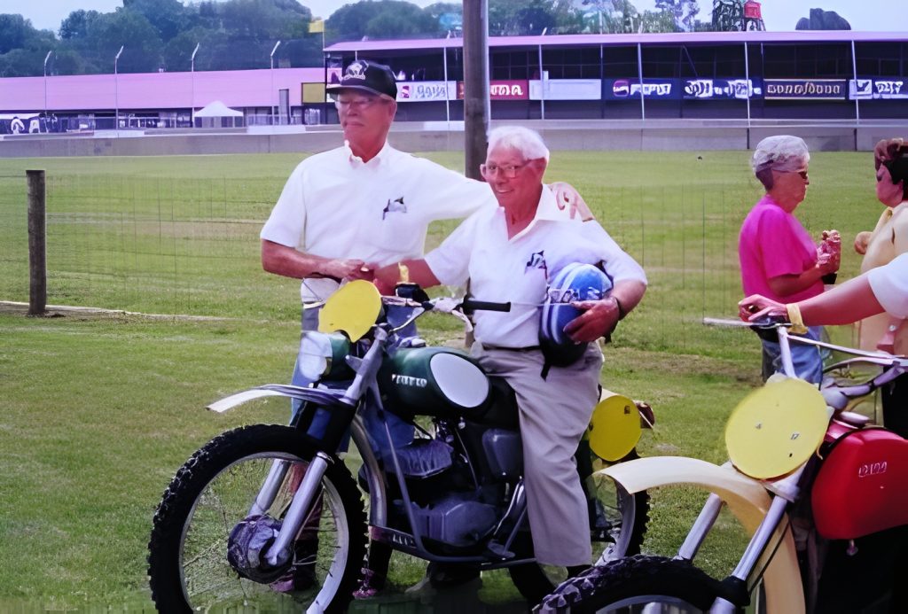 Two men with motorcycles at a racetrack event.
