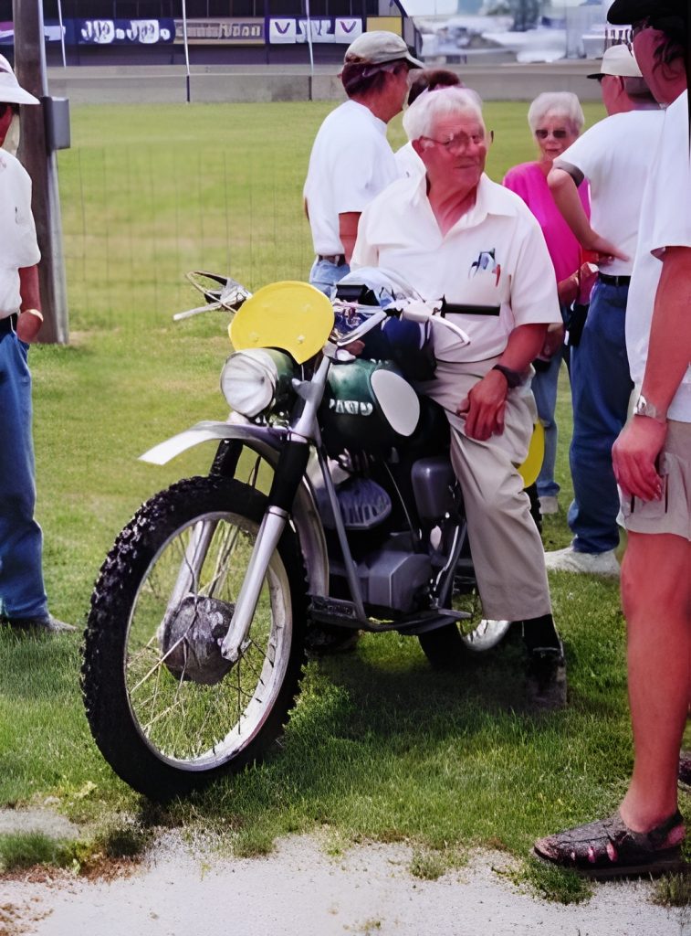 Man sitting on vintage motorcycle at outdoor event.