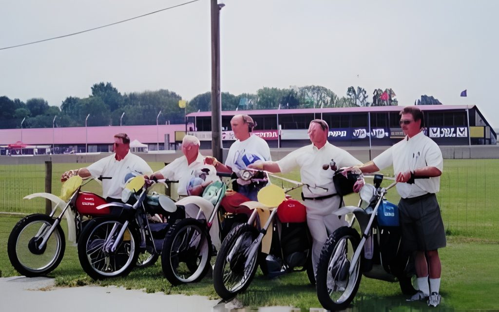 Five men standing with classic motorcycles outdoors.