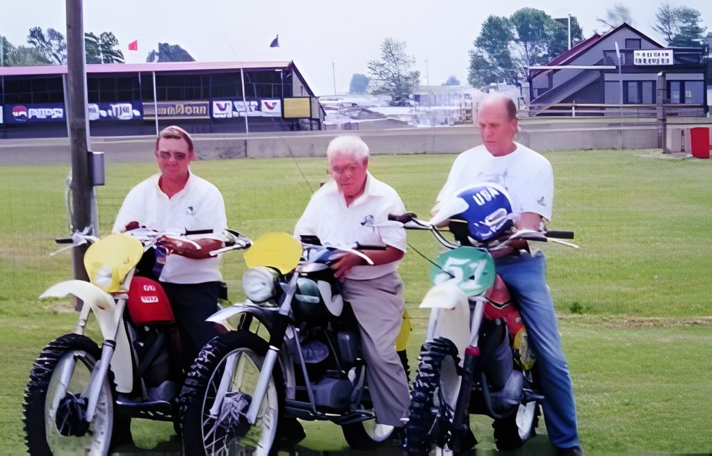 Three men on vintage motorcycles at a race track.
