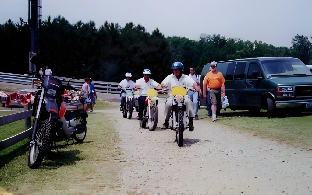 People and motorbikes near parked van at track