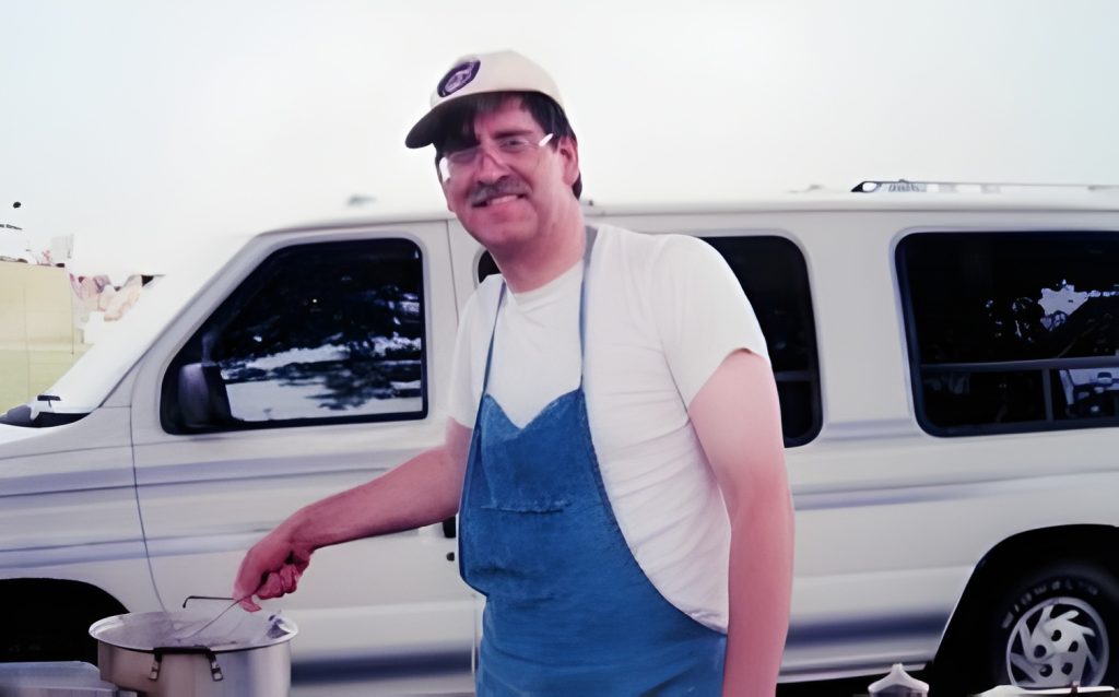Man cooking outdoors near a white van.