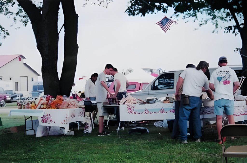 People browsing outdoor flea market with various items displayed.