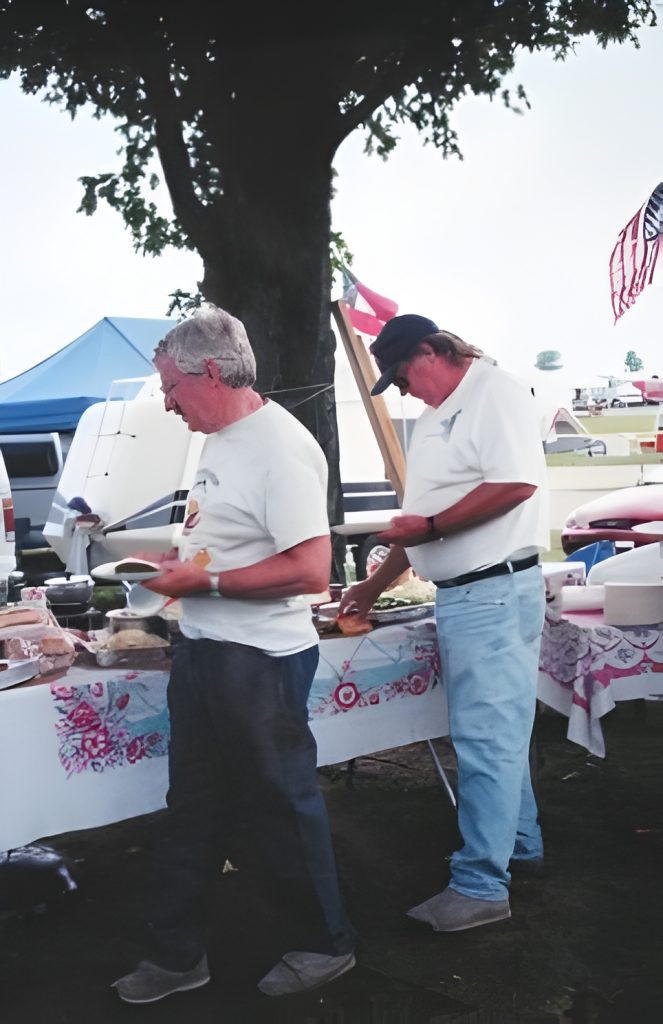 Two men making sandwiches at outdoor picnic table.