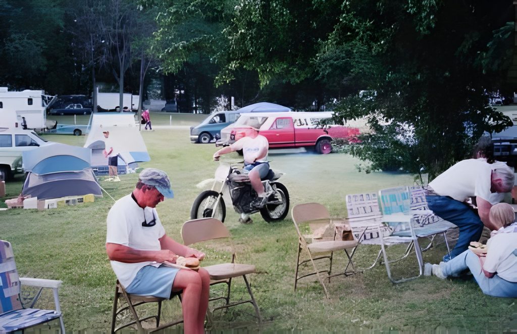 People camping with tents and vehicles in field.