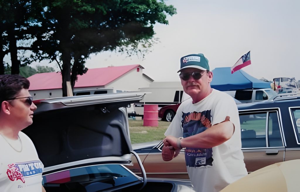 Two men near open car trunk at event.
