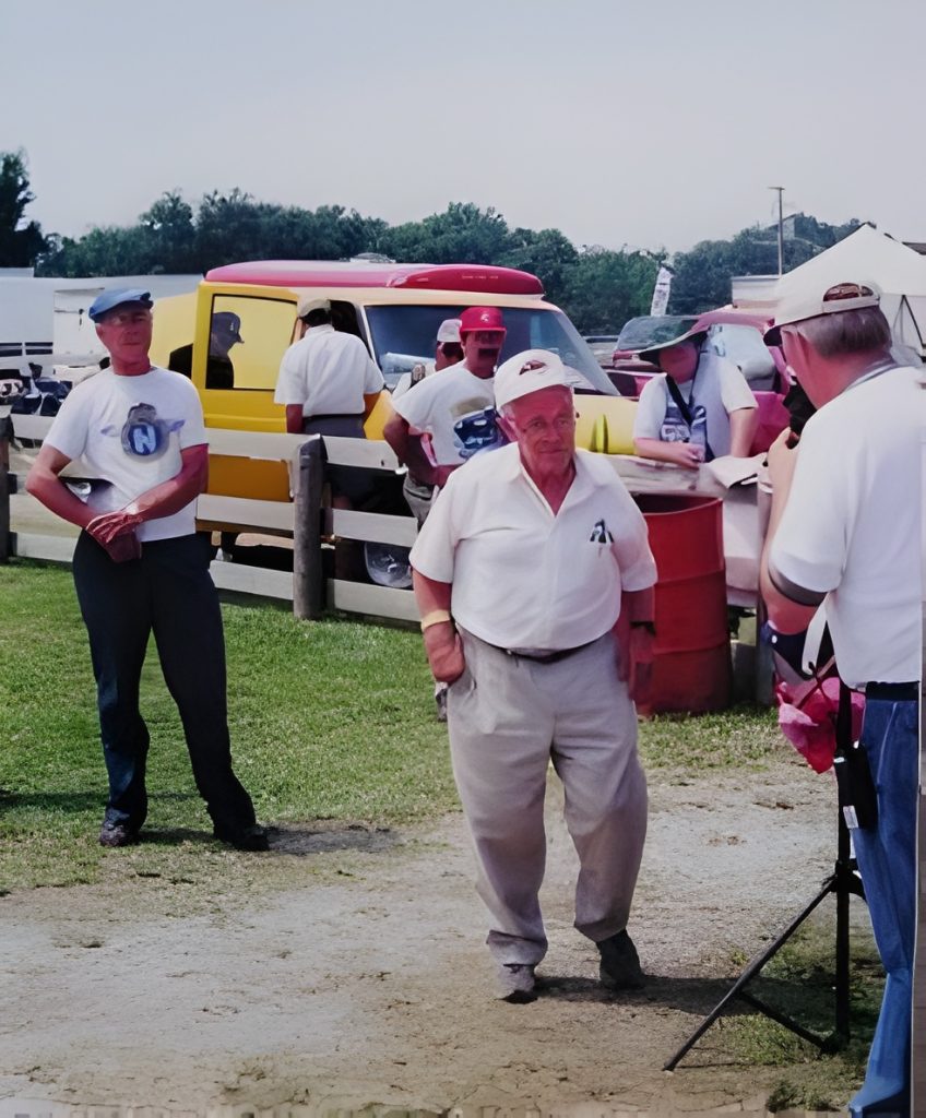 People gathered at an outdoor event near yellow vehicle.
