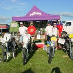 Group displaying vintage motorcycles under tent