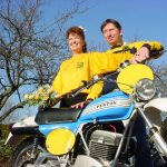Couple posing with vintage Penton motorcycle, sunny day.