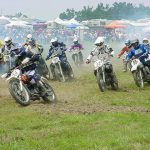 Dirt bike racers competing on grassy track under tents.