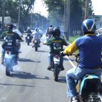 Group riding vintage motorcycles on a sunny street.
