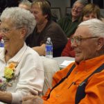 Elderly couple smiling in a crowd at an event.