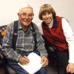 Smiling man and woman with notebook indoors.