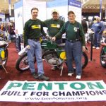Three men with vintage motorcycles at exhibition.