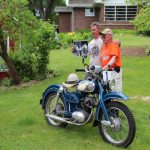 Two men posing with vintage motorcycle on grass