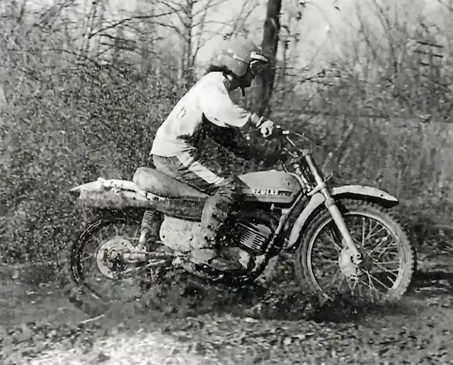 Motorcyclist riding through mud in the forest.