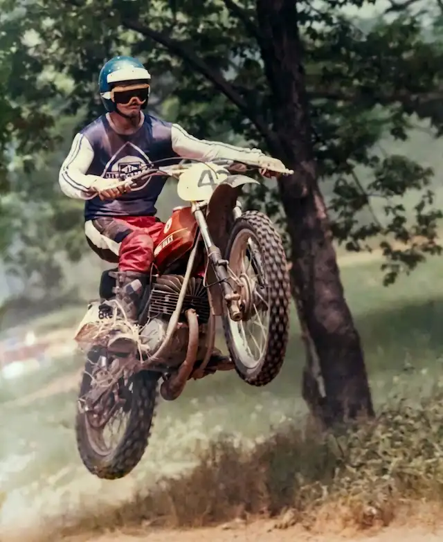 Motorcyclist jumps dirt bike in wooded area.