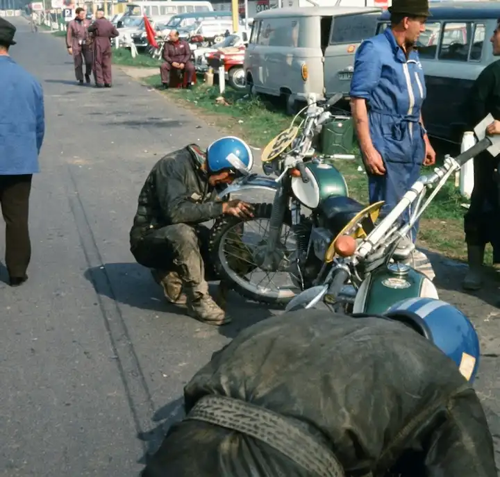 Motorcyclists repairing bikes at roadside event.
