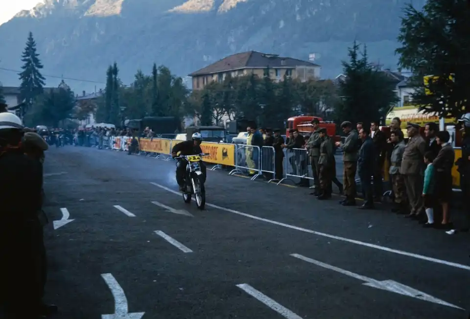 Motorcyclist racing in mountain town, crowd watching.