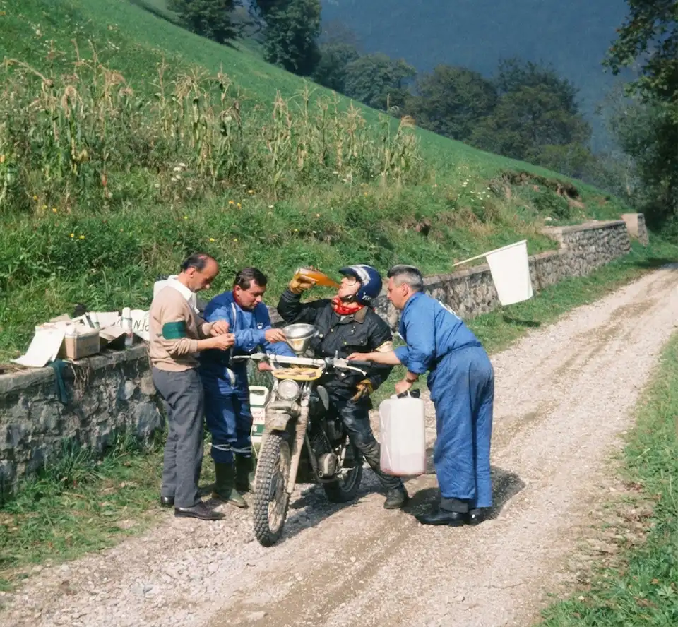 Men refueling motorcycle on countryside road.