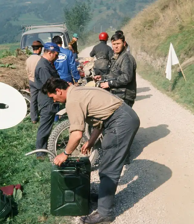 Men refueling motorcycles on rural dirt road.